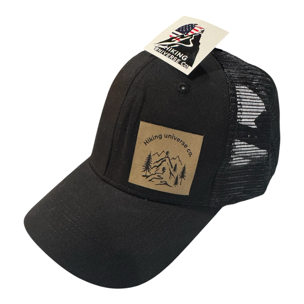 Black HIKING UNIVERSE CO. trucker hat with mesh back and faux leather patch featuring mountain landscape.