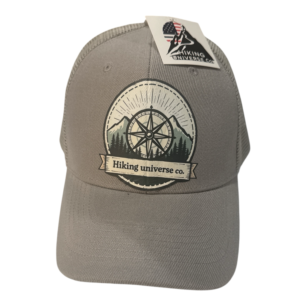 HIKING UNIVERSE CO. taupe trucker hat with embroidered compass, mountains, and trees patch.